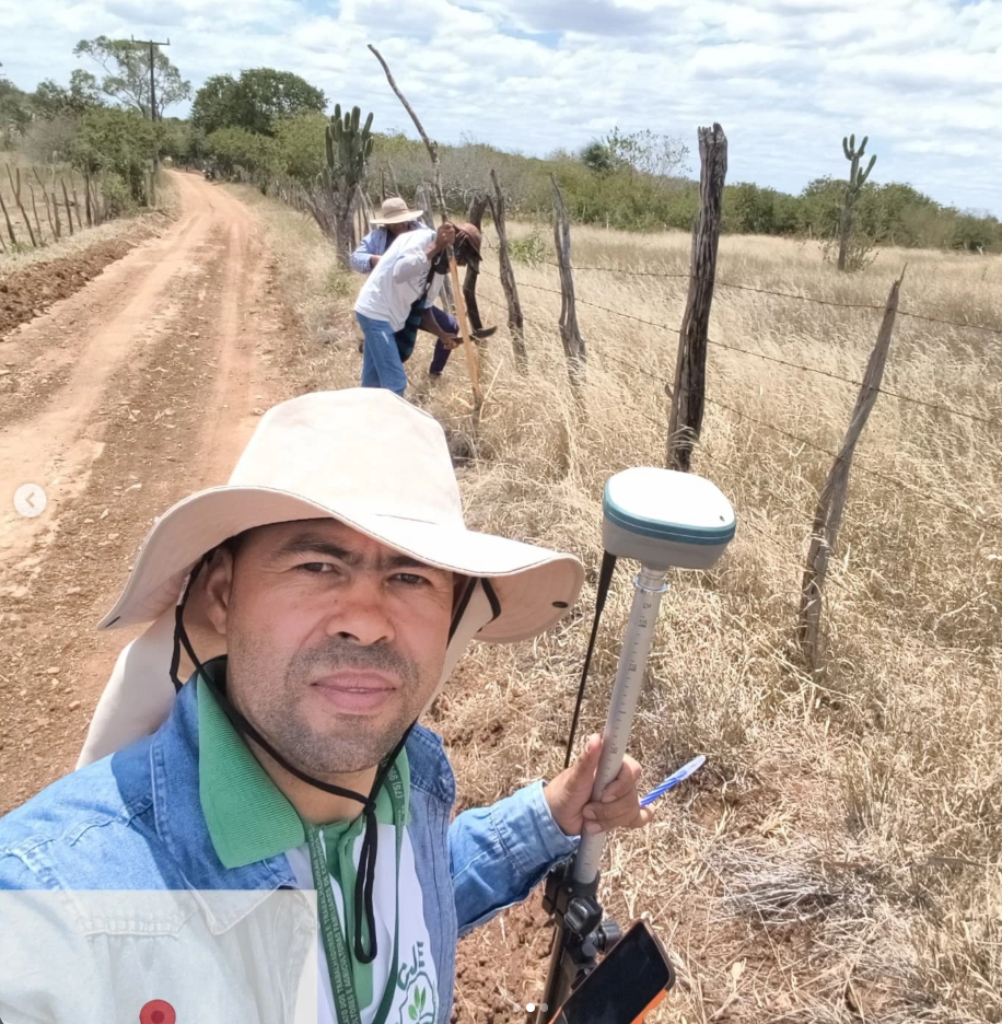 Responsável da CJE em campo com receptor GNSS ao lado de cerca em estrada rural